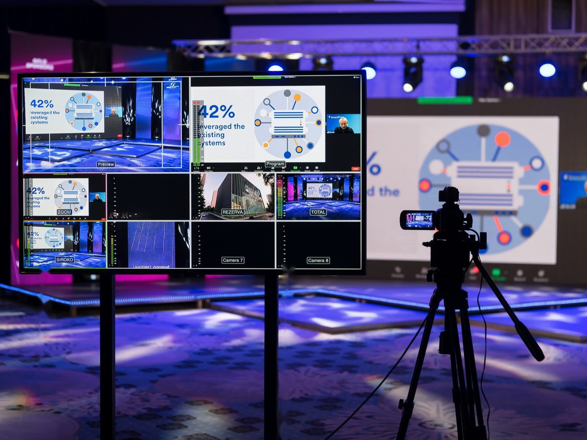 Multiview-Monitor und Kamera bei einer hybriden Konferenz mit Bühne und Leinwand